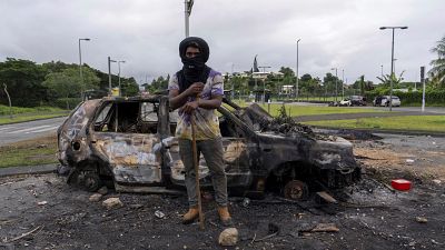 رجل يقف أمام سيارة محترقة بعد اضطرابات في نوميا، كاليدونيا الجديدة