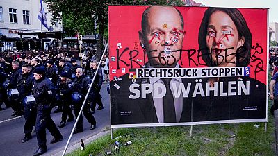 Police officers walk past a poster of the Social Democrats for the European elections during the revolutionary May Day demonstration in Berlin, Germany, Wednesday, May 1, 2024