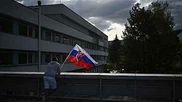 Un hombre ondea la bandera nacional de Eslovaquia frente al hospital donde tratan al primer ministro, Robert Fico