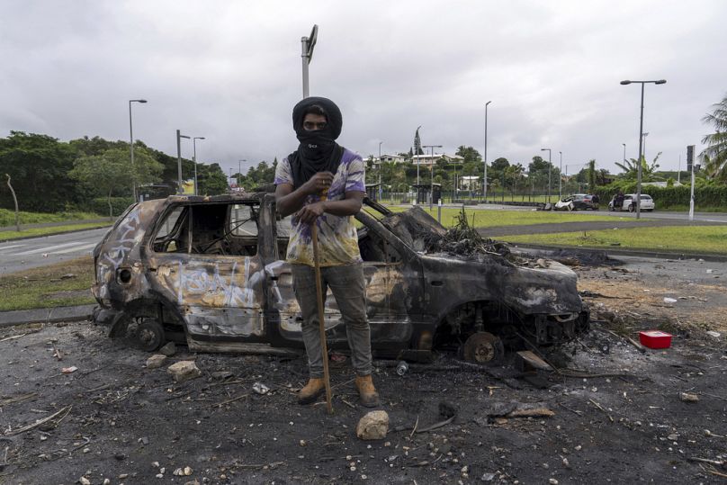 man stands in front a burnt car after unrest in Noumea, New Caledonia.