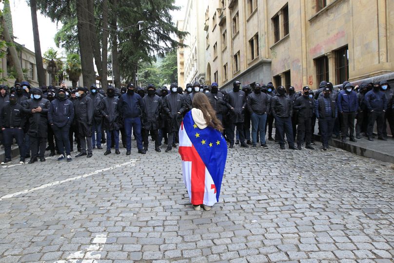 Ein Demonstrant mit drapierten georgischen National- und EU-Flaggen steht vor der Polizei, Georgien, Dienstag, 14. Mai 2024.