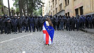 Ein Demonstrant mit drapierten georgischen National- und EU-Fahnen steht vor der Polizei, die den Weg zum Parlamentsgebäude in Tiflis blockiert, 14. Mai 2024