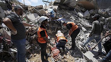 عمال إنقاذ فلسطينيون يحفرون حول جثة رجل تحت أنقاض مبنى دمر في غارة جوية إسرائيلية في النصيرات، غزة- 14 مايو، 2024.