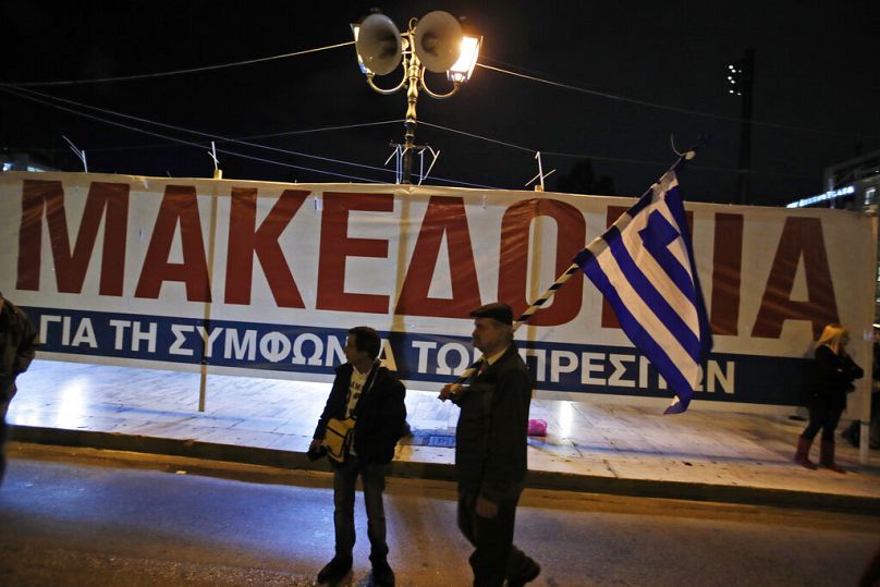 An opponent of Prespa Agreement holds a Greek flag, standing in front of a poster during a rally outside the Greek Parliament, January 2019
