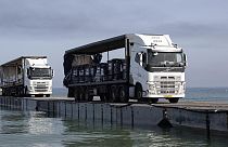 Gemiyle gelen yardımlar kamyonlarla yüzer bir geçit üzerinden kıyıya taşınıyor
