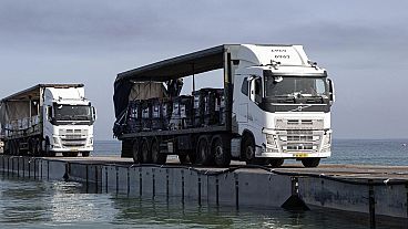 Gemiyle gelen yardımlar kamyonlarla yüzer bir geçit üzerinden kıyıya taşınıyor