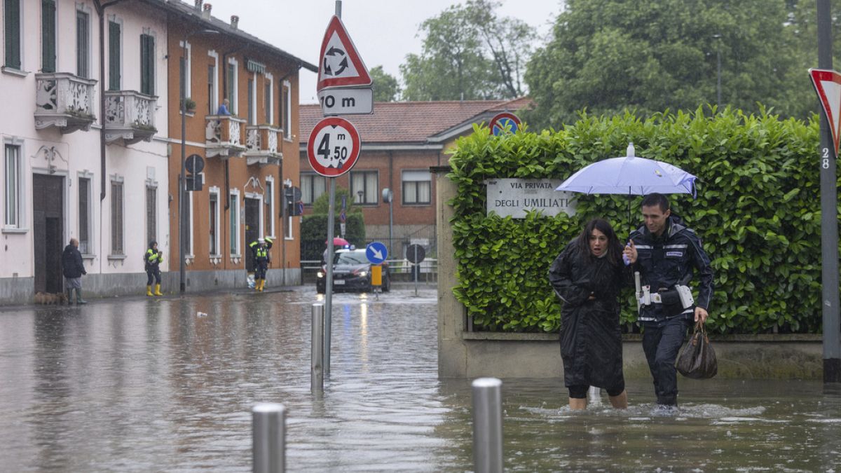 Bir şehir polisi, sağda, 15 Mayıs 2024 Çarşamba günü İtalya'nın Milano kentinde devam eden yağışların ardından şehrin bir kısmının sular altında kalmasının ardından bir kadının yolun karşısına geçmesine yardım ediyor 