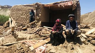 Afgan bir çift, 18 Mayıs 2024 Cumartesi günü Afganistan'ın batısındaki Ghor vilayetinde meydana gelen şiddetli sel felaketinin ardından hasar gören evlerinin yakınında oturuyor.