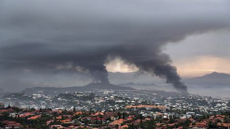 Дым над Нумеа, Новая Каледония, 15 мая 2024 г. Используя экскаваторы, власти расчистили дорогу в аэропорт от обгоревших автомобилей в воскресенье.
