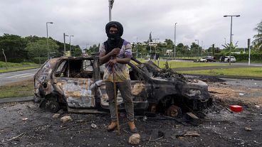 رجل يقف أمام سيارة محترقة بعد أعمال عنف 
