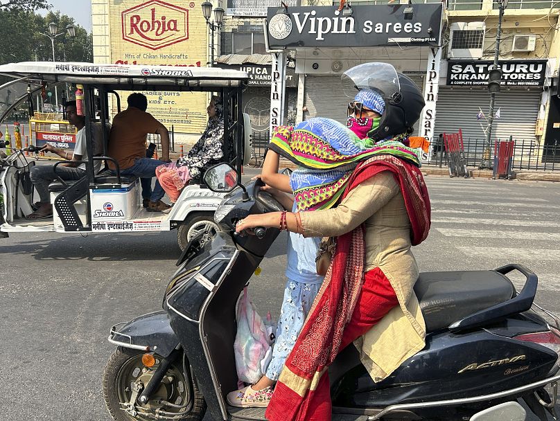 A rider covers her daughter's head with a scarf to protect her from severe heat in Lucknow, India, 18 May 2024.