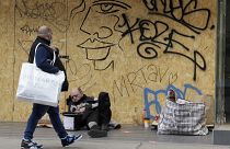 Un hombre que lleva una bolsa de compras pasa junto a un hombre sin hogar en el suelo junto a una tienda cerrada en Oxford Street en Londres, el lunes 12 de abril de 2021.