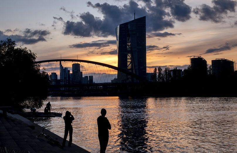 Menschen stehen am Mainufer in der Nähe der Europäischen Zentralbank in Frankfurt, nach Sonnenuntergang am Montag, 22. April 2024