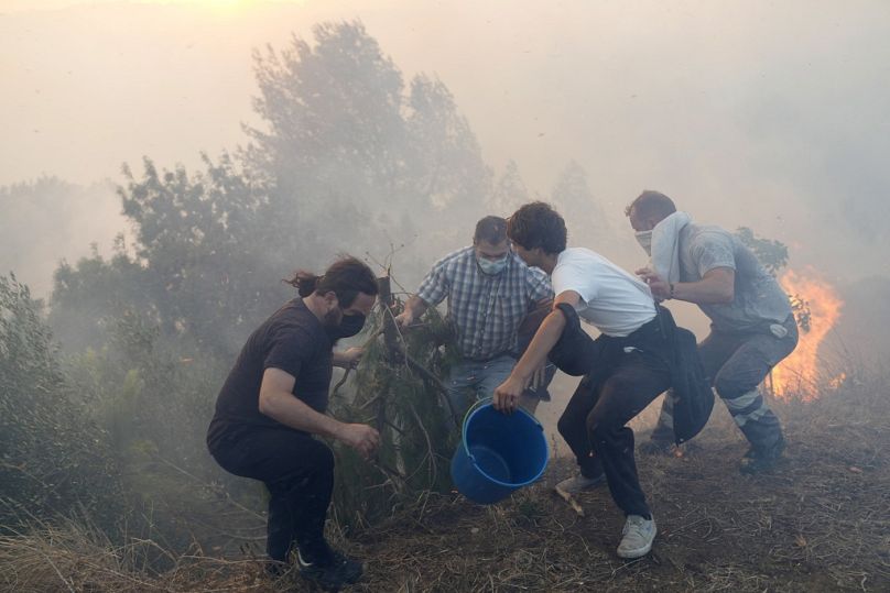 Local residents use buckets with water to try to slow down flames approaching their houses in Alcabideche, outside Lisbon, Portugal in July 2023