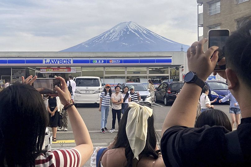 Des touristes prennent des photos devant la supérette Lawson, un lieu de photo populaire encadrant une vue pittoresque du mont Fuji en arrière-plan, le 30 avril 2024.