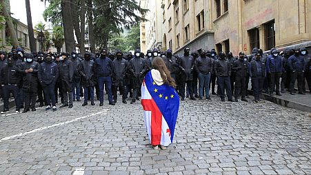 Una donna tiene in mano una bandiera nazionale georgiana e una dell'Ue mentre protesta contro la "legge russa" vicino al palazzo del Parlamento a Tbilisi, in Georgia