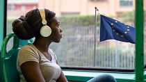 Mujer escuchando música frente a una bandera europea.