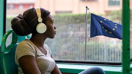 Mujer escuchando música frente a una bandera europea.