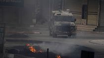 مركبة إسرائيلية تتحرك بالقرب من إطارات مشتعلة خلال اشتباكات مع متظاهرين فلسطينيين في مدينة جنين بالضفة الغربية، الأربعاء، 22 مايو، 2024