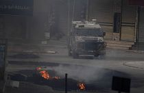 مركبة إسرائيلية تتحرك بالقرب من إطارات مشتعلة خلال اشتباكات مع متظاهرين فلسطينيين في مدينة جنين بالضفة الغربية، الأربعاء، 22 مايو، 2024