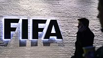 In this Dec. 2, 2015 photo a man stands in front of the logo at the FIFA headquarters "Home of FIFA" in Zurich, Switzerland. (Walter Bieri/Keystone via AP)