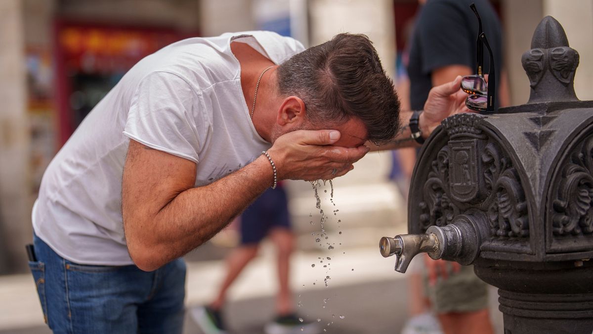 Un uomo si rinfresca in una fontana durante una calda e soleggiata giornata estiva a Madrid, in Spagna.