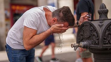 Un hombre se refresca en una fuente durante un caluroso y soleado día de verano en Madrid, España.