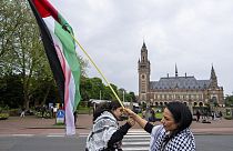 Dos manifestantes ondean la bandera palestina frente al Palacio de la Paz, en la parte trasera, que alberga el Tribunal Internacional de Justicia, o Tribunal Mundial, en La Haya, mayo de 2024.