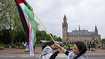 Két tüntető lengeti a palesztin zászlót a Nemzetközi Bíróságnak (Világbíróság) otthont adó Békepalota előtt Hágában, 2024 májusában.