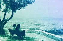 Two women sit on a bench overlooking the Greek capital as a haze of dust blown over from North Africa covers the city, in Athens, May 2024