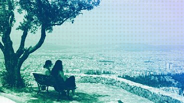 Two women sit on a bench overlooking the Greek capital as a haze of dust blown over from North Africa covers the city, in Athens, May 2024