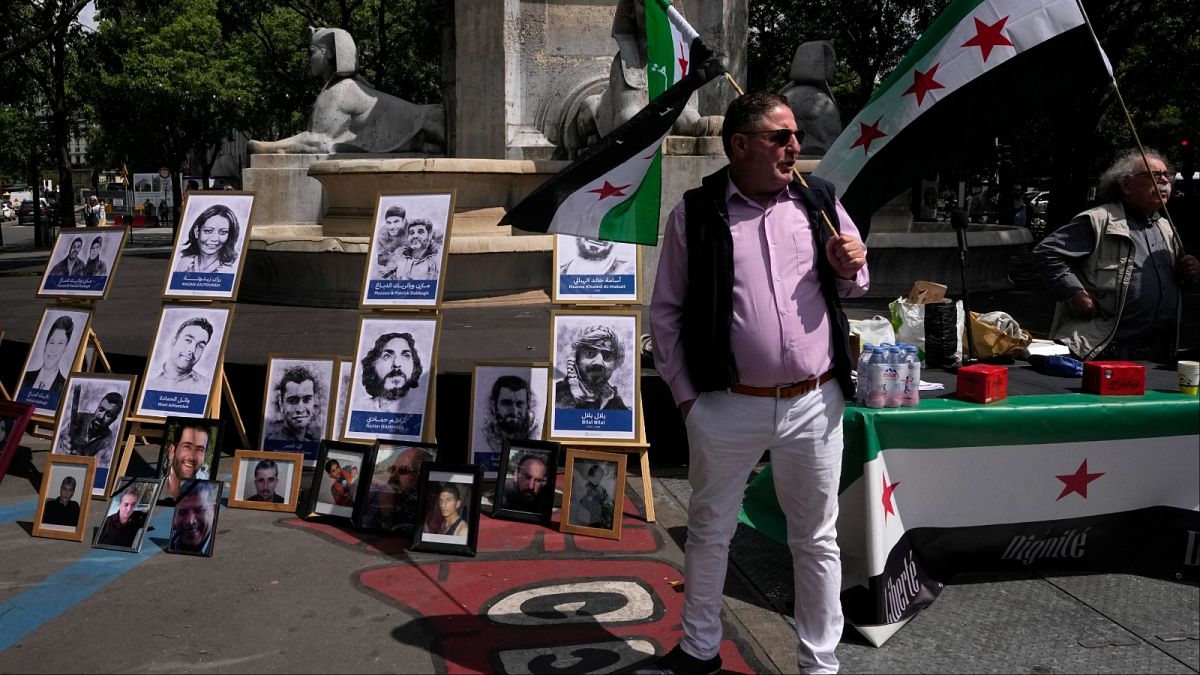 نشطاء يحملون الأعلام السورية بجانب صور ضحايا للنظام السوري، خلال مظاهرة الثلاثاء 21 مايو 2024 أمام المحكمة في باريس