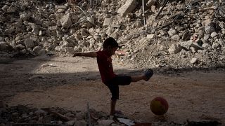 طفل فلسطيني يلعب بالكرة بجانب مبنى دمره الجيش الإسرائيلي في جنين