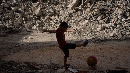 طفل فلسطيني يلعب بالكرة بجانب مبنى دمره الجيش الإسرائيلي في جنين