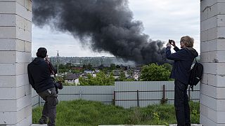 Jornalistas estrangeiros fazem uma reportagem a partir de um ponto de observação enquanto se levanta fumo após um ataque russo em Kharkiv, na Ucrânia, na sexta-feira, 17 de maio de 2024.
