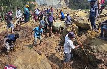 Aldeões procuram por entre um deslizamento de terras em Yambali, nas terras altas da Papua Nova Guiné, domingo, 26 de maio de 2024.
