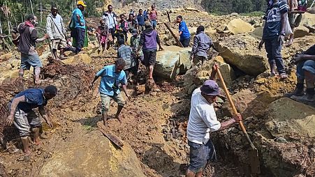 Aldeões procuram por entre um deslizamento de terras em Yambali, nas terras altas da Papua Nova Guiné, domingo, 26 de maio de 2024.