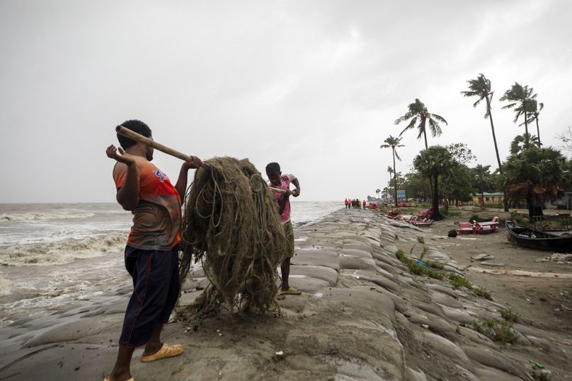رجال ينقلون شباك الصيد بينما تتدفق المياه إلى شاطئ كواكاتا على ساحل خليج البنغال بسبب تقدم إعصار ريمال في باريسال، بنغلاديش، 26 مايو 2024