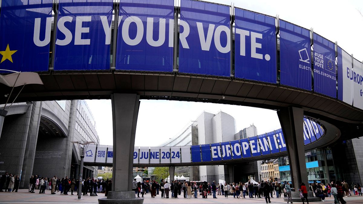 مردم در صف انتظار برای بازدید از پارلمان اروپا در جشن «روز اروپا» در بروکسل در ۴ مه ۲۰۲۴ و تیلیغاتی که بر روی آن نوشته «از رای خود استفاده کنید.».