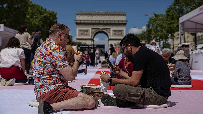 Two men eat their lunch as part of a giant picnic on the Champs-Elysées, in front of the Arc de Triomphe, organized by the Comité Champs-Élysées, Sunday, May 26, 2024 in Pari