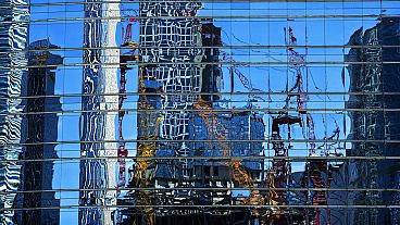 Cranes at a construction site in the Central Business District are reflected on a window panels of an office building in Beijing, Sunday, May 26, 2024. 