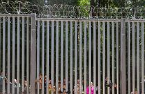 Members of a group of some 30 migrants seeking asylum look through the railings of a wall that Poland has built on its border with Belarus to stop massive migrant pressure.