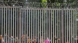 Members of a group of some 30 migrants seeking asylum look through the railings of a wall that Poland has built on its border with Belarus to stop massive migrant pressure.