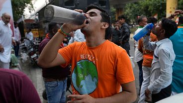 Um homem bebe água numa banca à beira da estrada que serve água potável gratuita aos passageiros, numa altura em que a vaga de calor continua a assolar a capital indiana, Nova Deli.