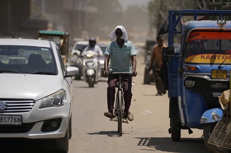 Um homem cobre o rosto com um pano para se proteger do calor enquanto anda de bicicleta numa rua movimentada de Jammu, na Índia.