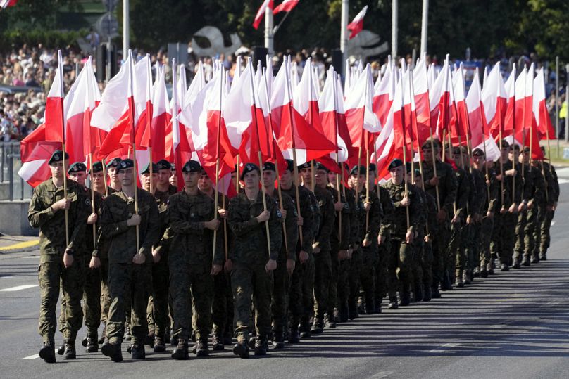 Membros das novas tropas voluntárias de Defesa Territorial marcham com as bandeiras nacionais da Polónia