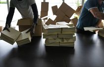 Imagen en la que se puede ver a dos personas ordenando numerosas papeletas electorales.