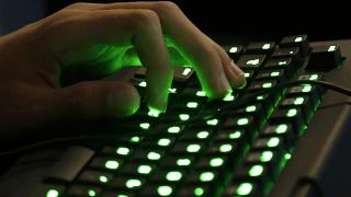 A mão de uma pessoa pousa sobre um teclado iluminado.