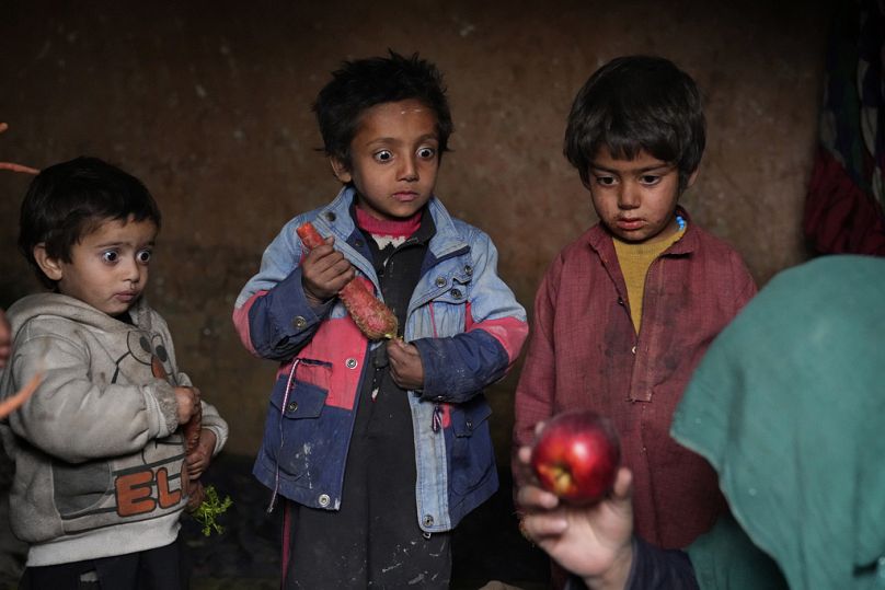Three Afghan internally displaced children look with surprise at an apple that their mother brought home after begging, in a camp on the outskirts of Kabul, February 2023