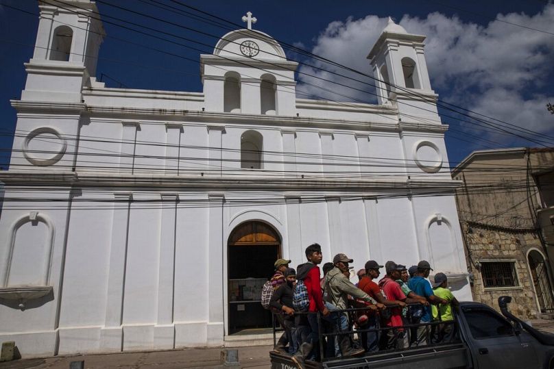 Workers commuting to work in the truck bed of a pickup, ride past the Cathedral in downtown Copan Ruinas, July 2021
